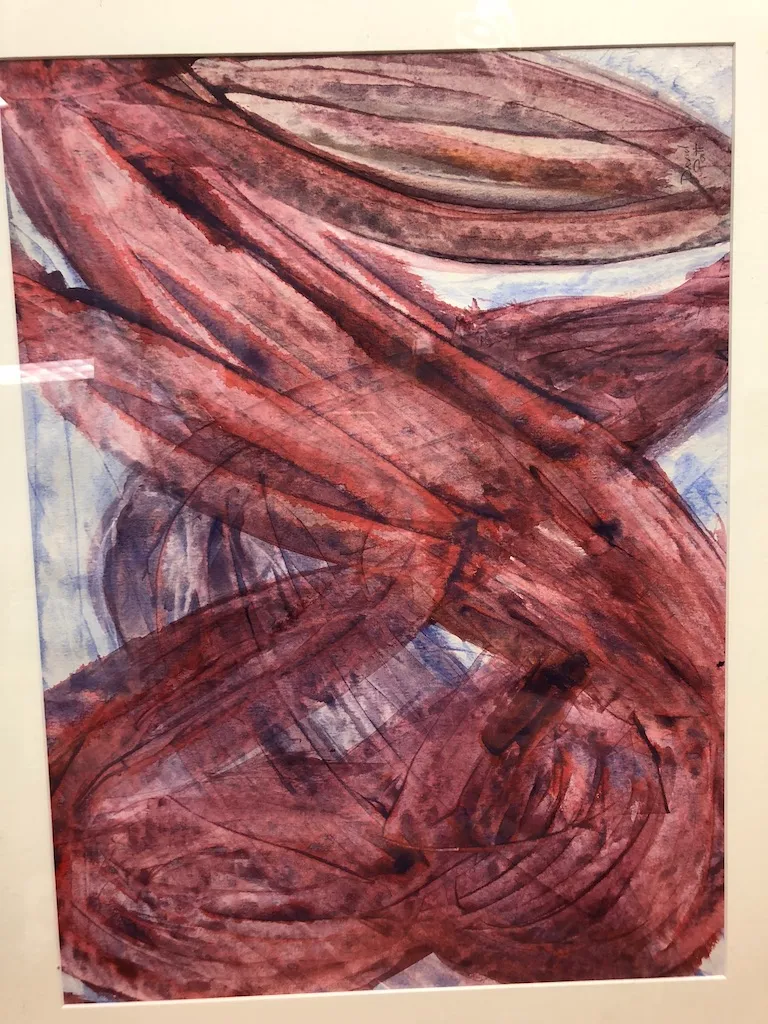 A framed painting of overlapping red-brown bands crossing a pale blue ground.