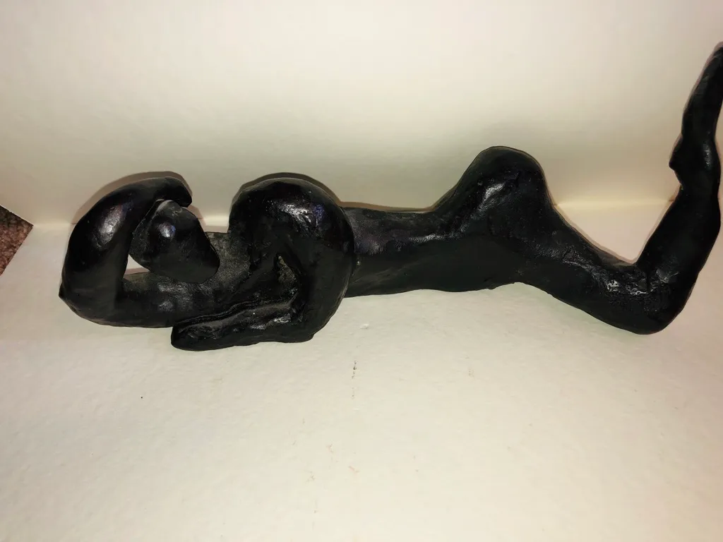 The black reclining figure lit from above, its surface glossy.
