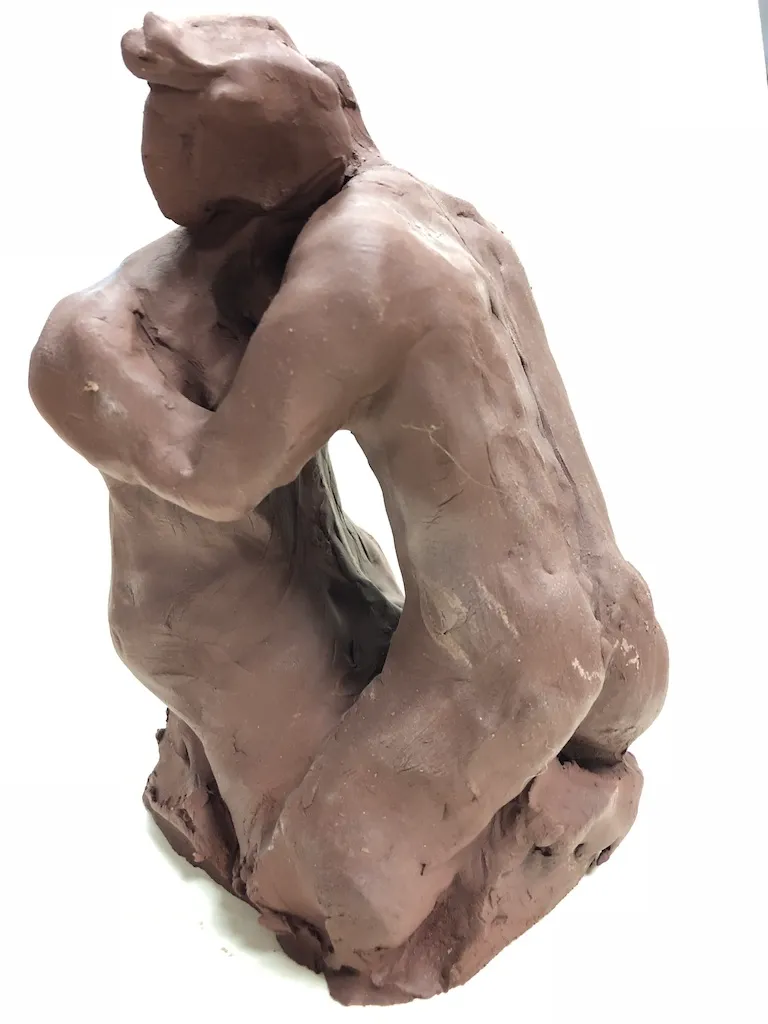The kneeling clay figure from the side, the curve of its back running down to the base.