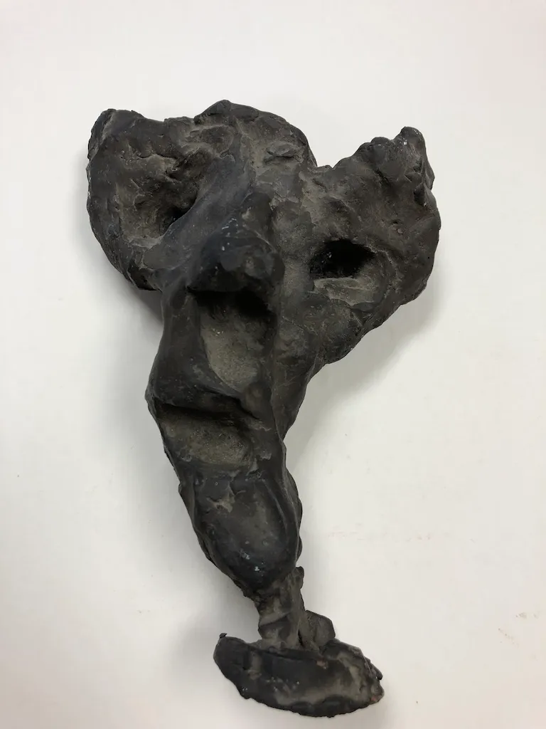 A dark clay torso with deep hollows at the eyes and chest, ending in one leg and a foot.