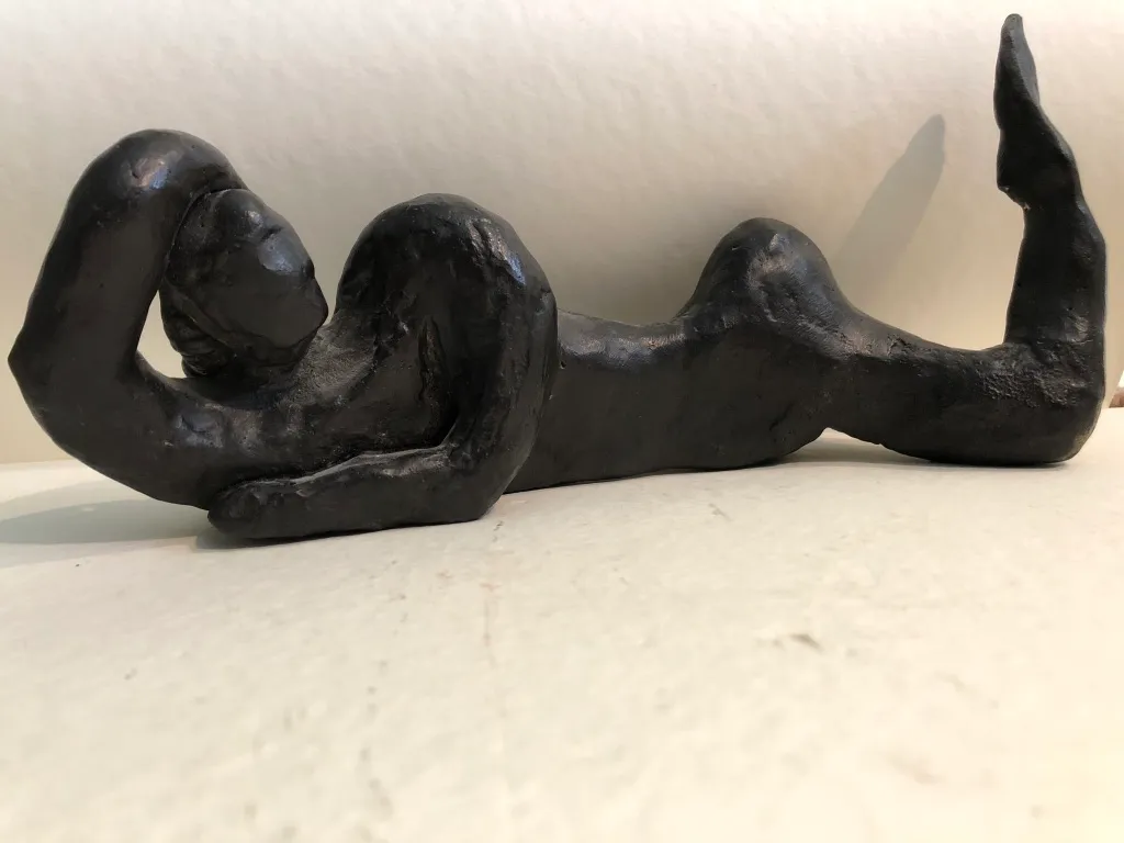 A black clay figure lying back with one leg lifted, photographed close.