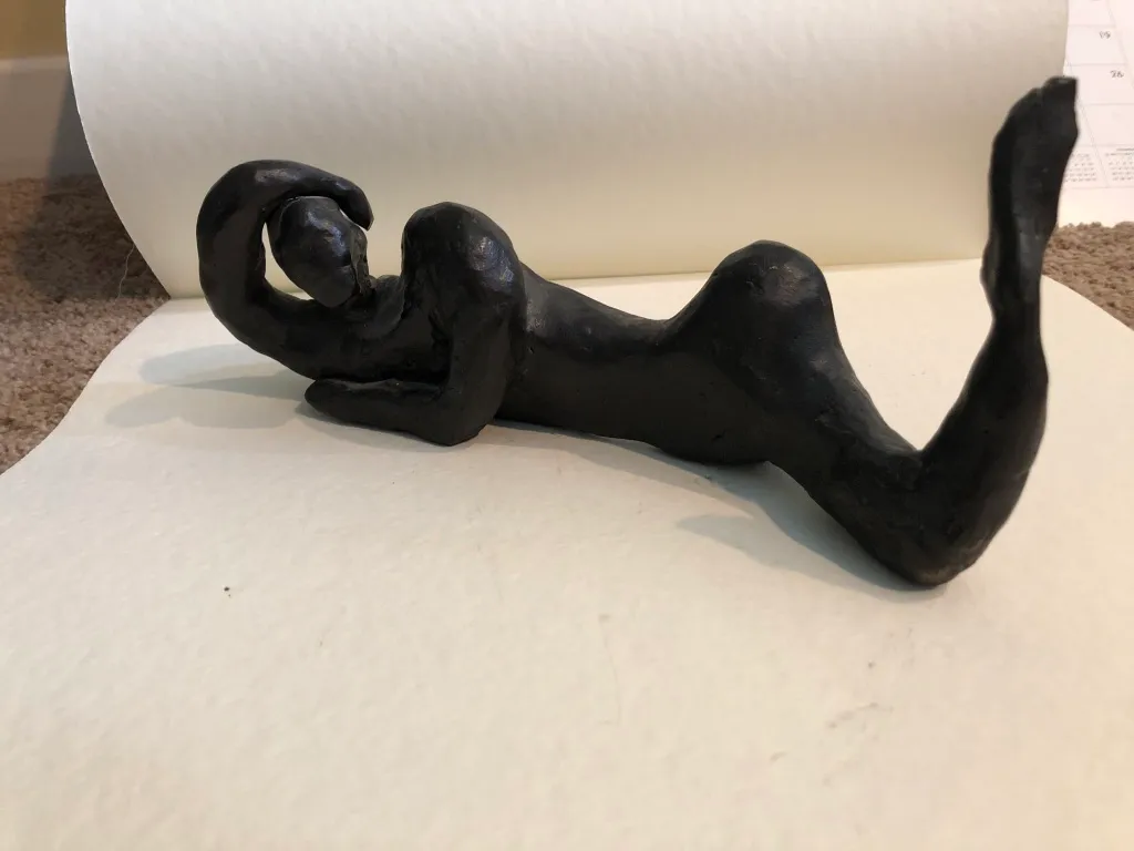 The black reclining figure resting against a roll of paper, seen from the front.