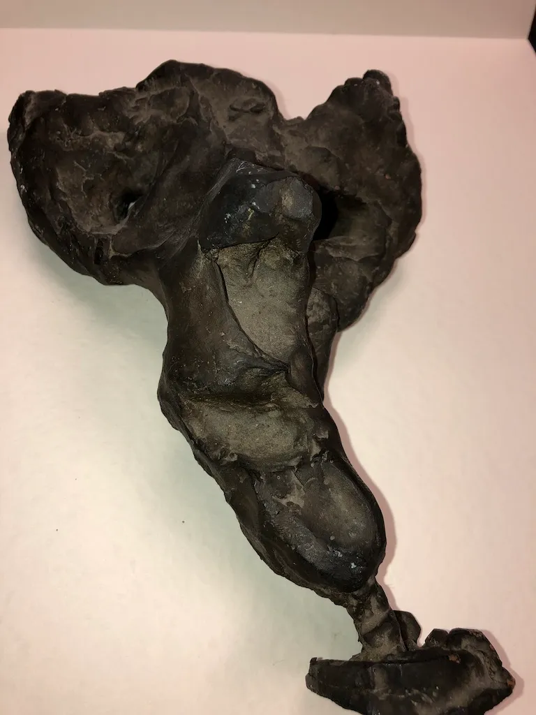 A dark clay torso against a pale pink wall, broken open at the chest.