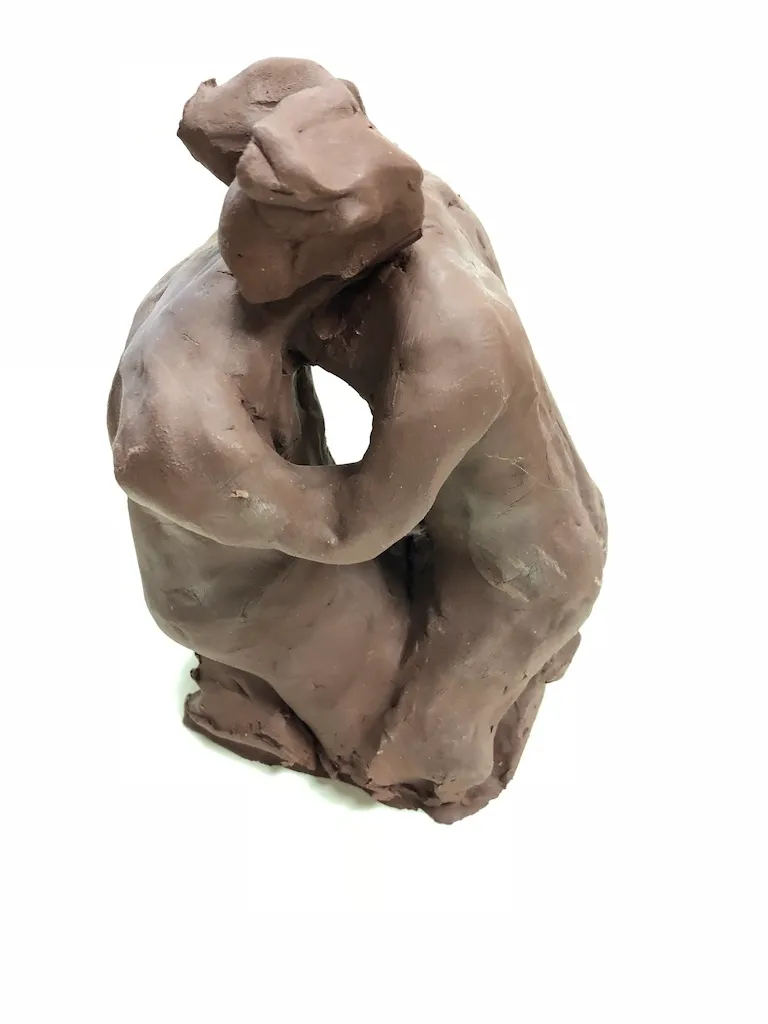 The kneeling clay figure against white, an opening showing through its folded arms.