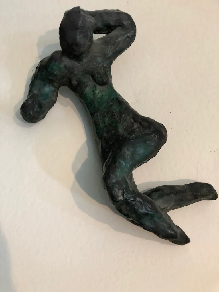 The green-patinated reclining figure on a white wall, seen from above.